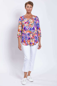 Full front view of a woman modeling a vibrant floral top with white pants