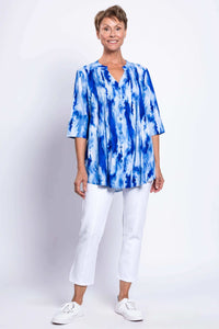 Full front view of a woman in a blue tie-dye Margate blouse paired with white pants