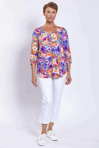 Full front shot of model in vibrant floral Jazz top paired with white pants