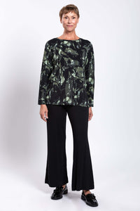Straight full front view of a woman in a green and black bamboo print top and black pants