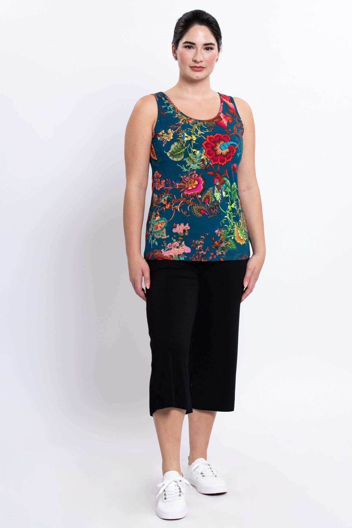 Full front view of a woman modeling a teal floral Avalon tank with black pants and white sneakers