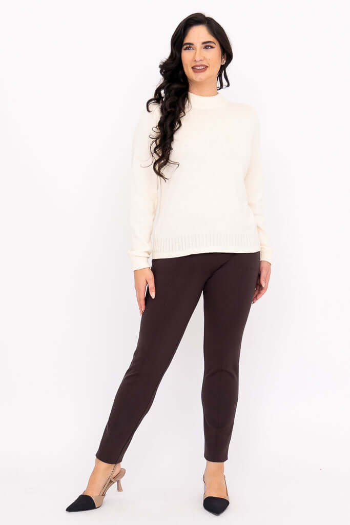 Woman standing straight in cream sweater and brown pants, front view