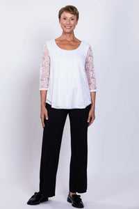 Full front view of a woman modeling a white lace overlay top with black pants and black shoes