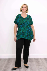 Full front view of woman standing in green and blue leafy print tunic top and black pants