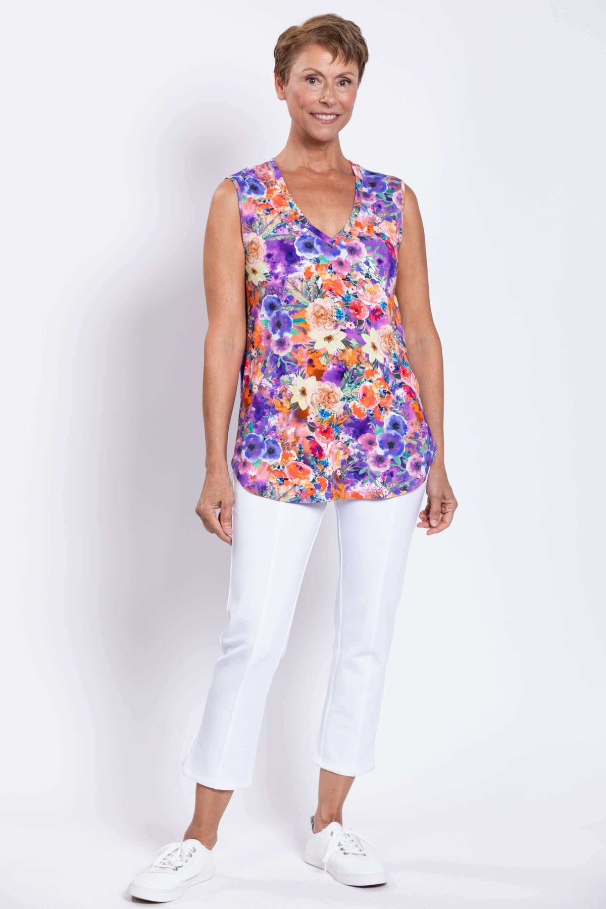 Full front view of a woman in a vibrant sleeveless floral top and white pants