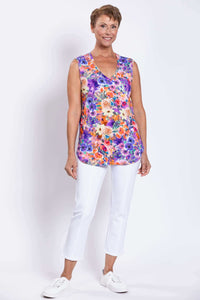 Full front view of a woman in a vibrant sleeveless floral top and white pants