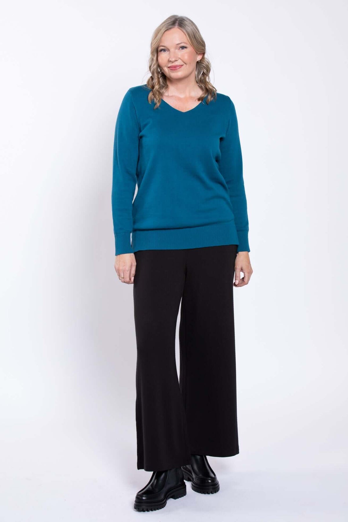 Woman standing in black wide-leg pants and a teal sweater, front view