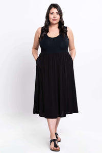 Full front view of a woman in a black sleeveless empire waist midi dress with hands in pockets