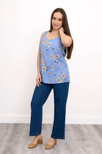 Woman in blue floral sleeveless top and jeans smiling with hand on neck