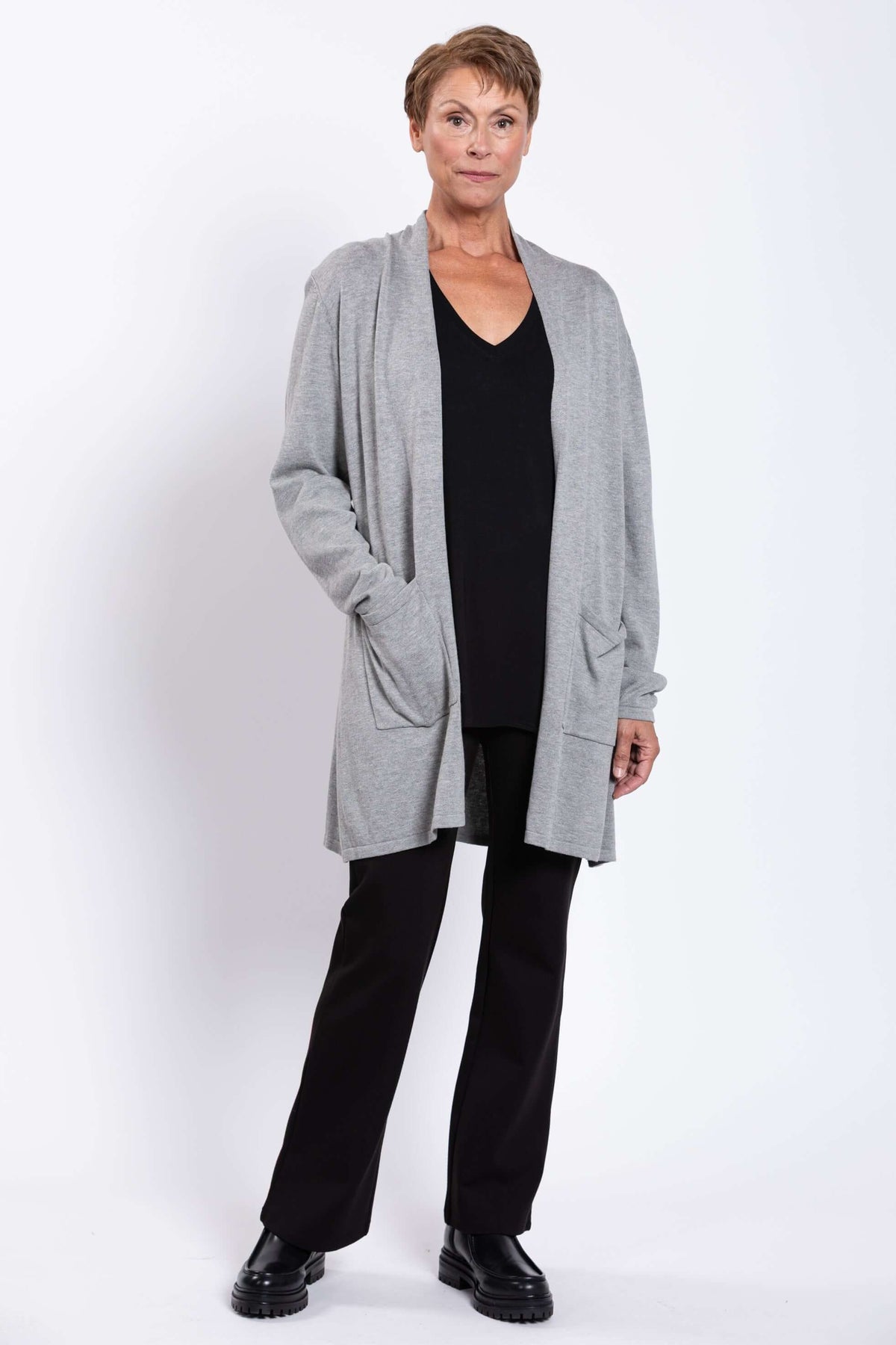 Full front view of a woman modeling a grey cardigan over black outfit and boots