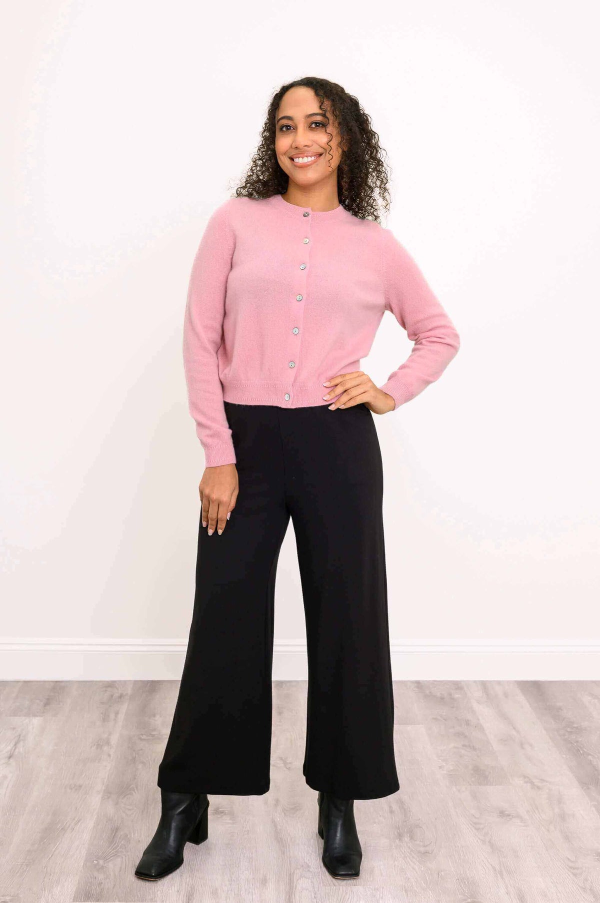 Full front view of model in pink cashmere cardigan, black pants, and ankle boots