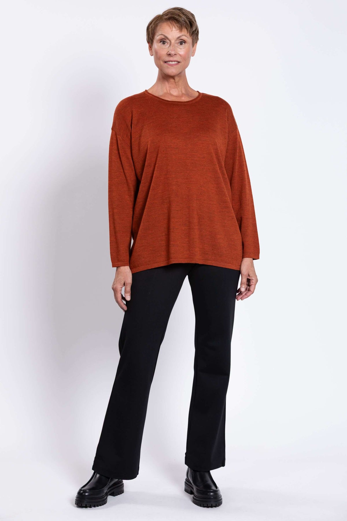 Full front view of woman modeling rust red Merino wool sweater and black pants
