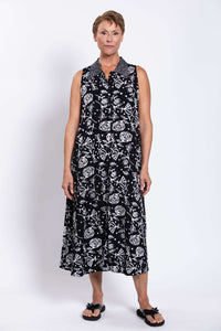Full front view of a woman in a sleeveless black swing shirt dress with white graphic floral print