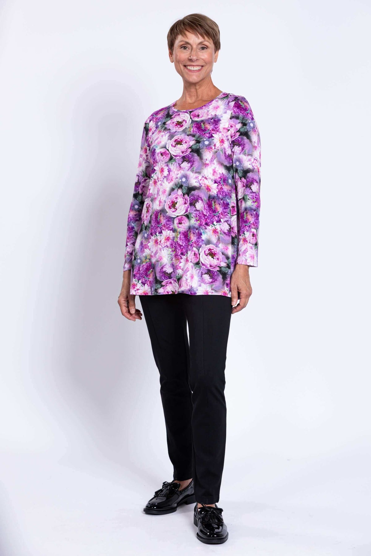 Full body front view of woman in floral tunic top with black pants