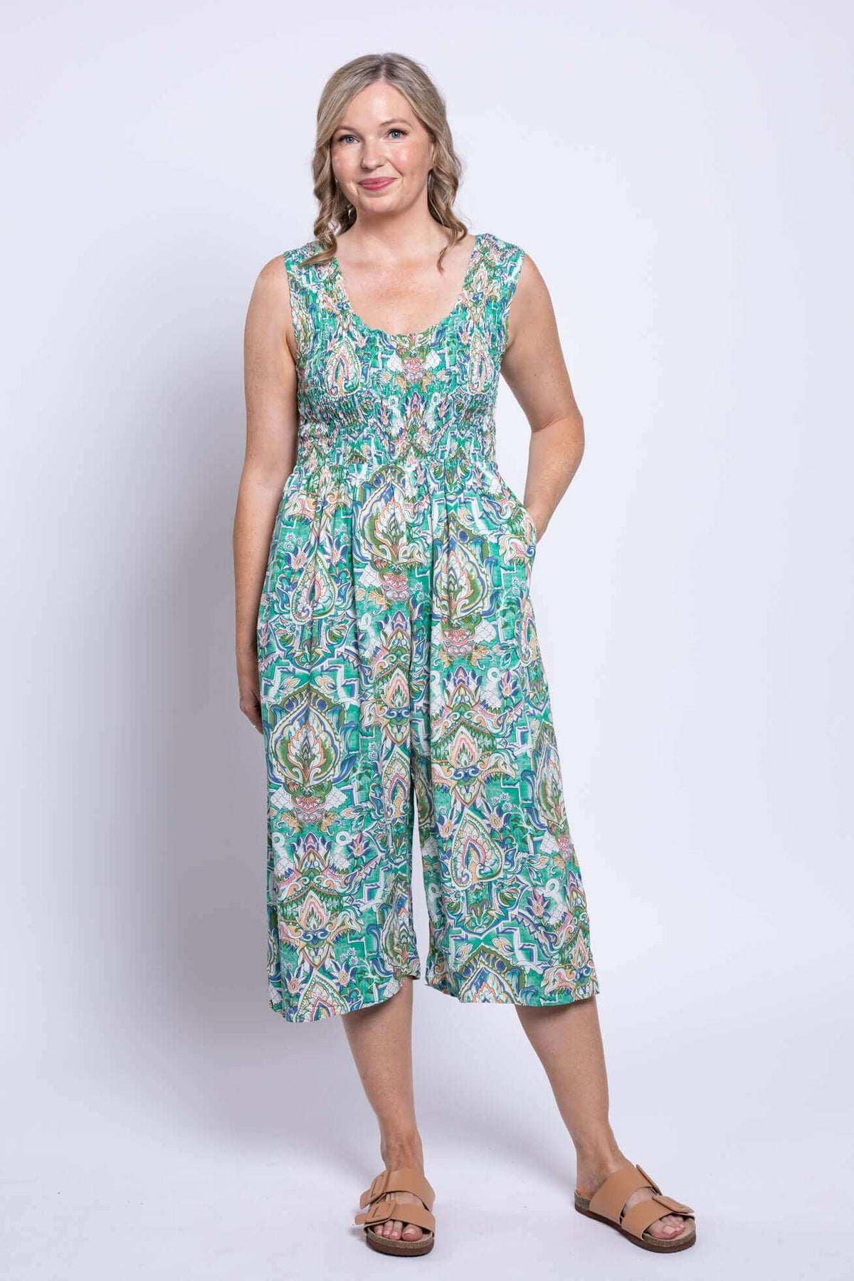 Full front view of woman in patterned shirred jumpsuit with hands in pockets
