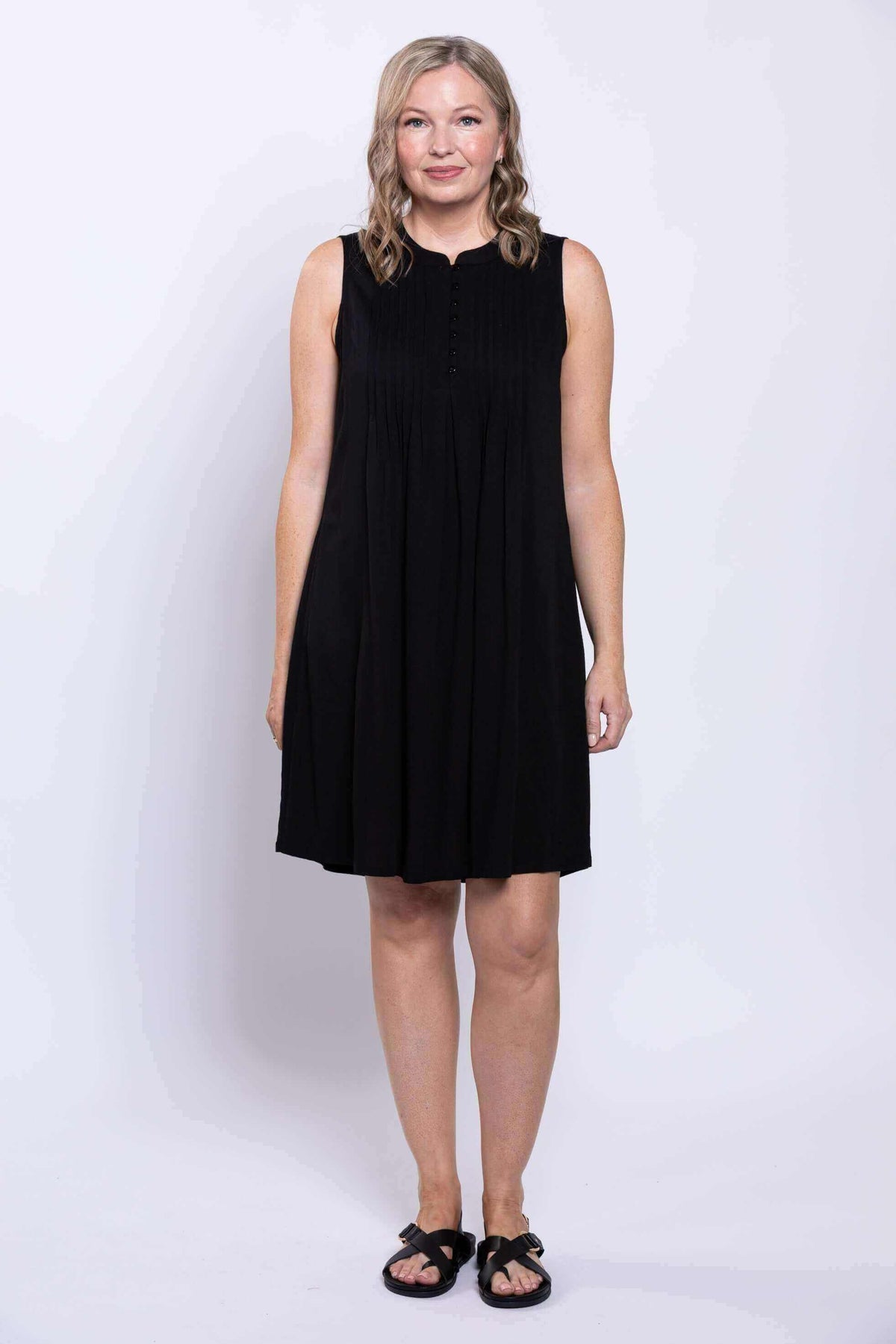 Full front view of woman in sleeveless black pintuck knee-length dress