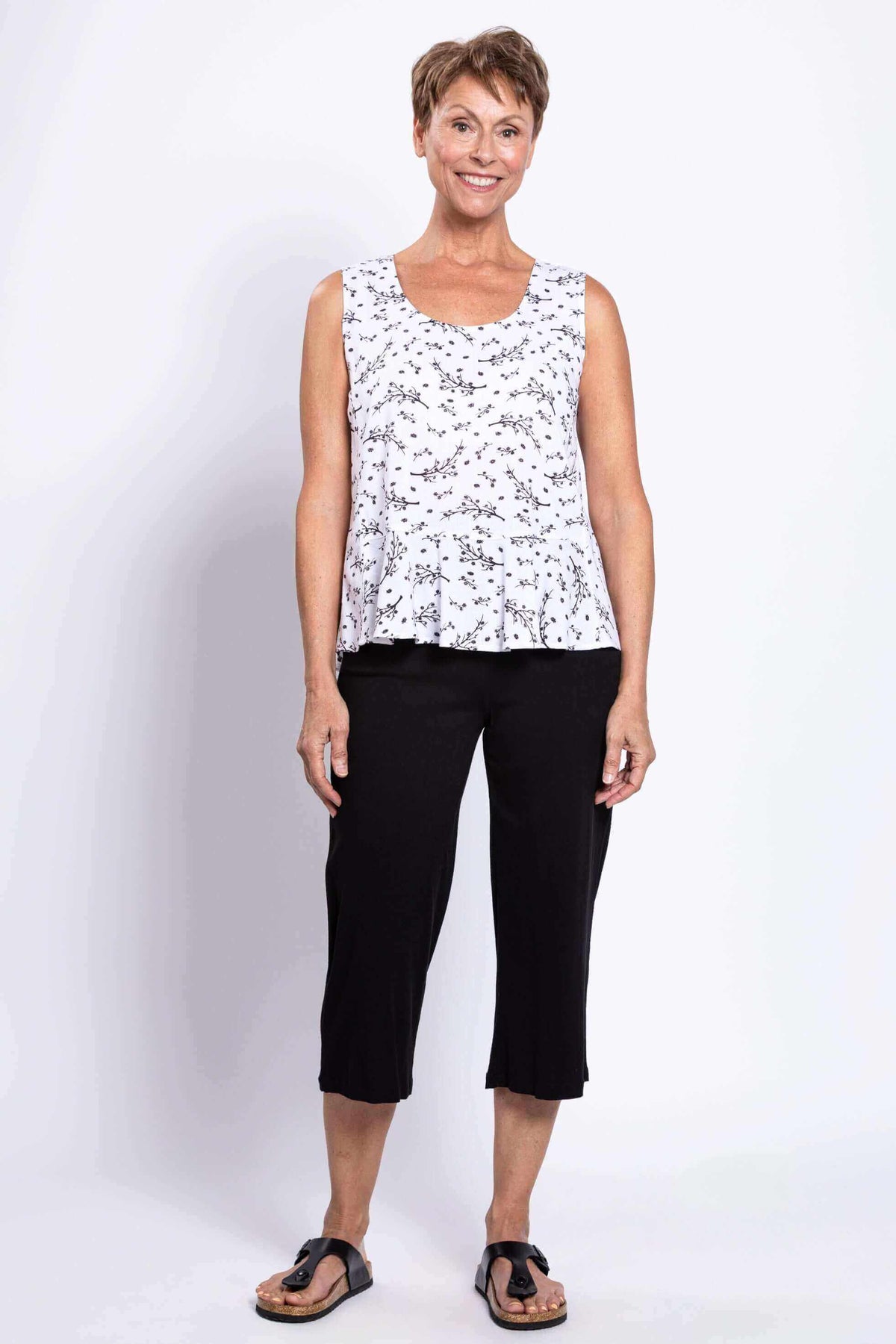 Full front view of woman in white floral peplum tank and black pants