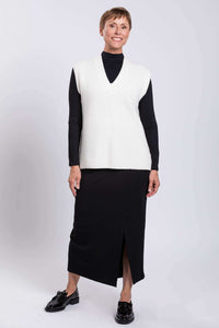 Full front view of woman modeling white V-neck sweater vest paired with black skirt