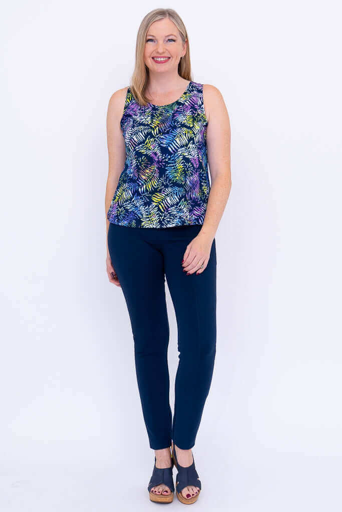 Full body front view of woman in colorful fern print tank and navy pants