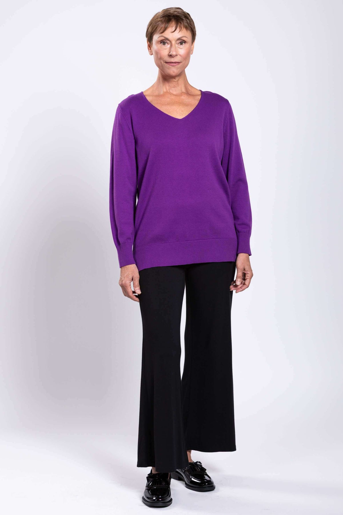 Frontal full length view of model in purple V-neck sweater and black pants