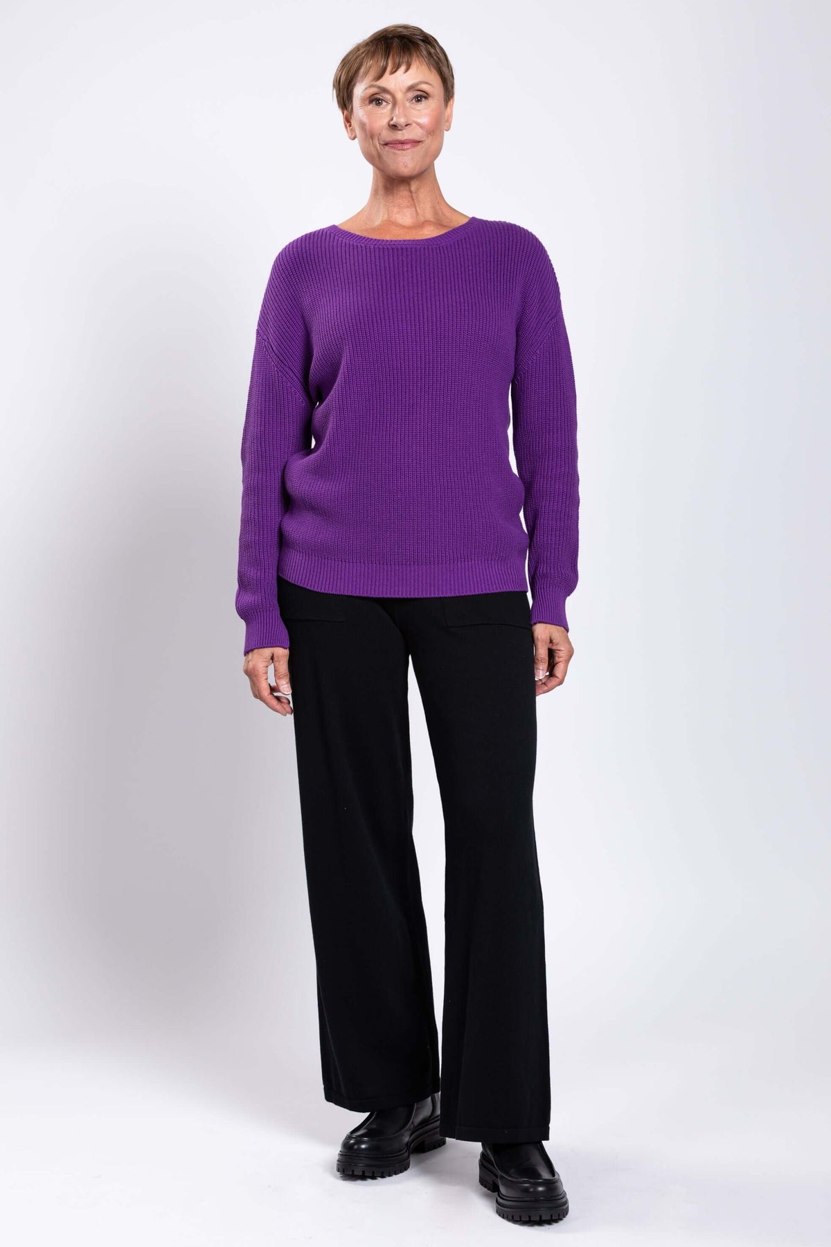 Full length front view of a woman in a purple shaker stitch sweater and black pants