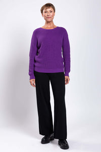 Full length front view of a woman in a purple shaker stitch sweater and black pants