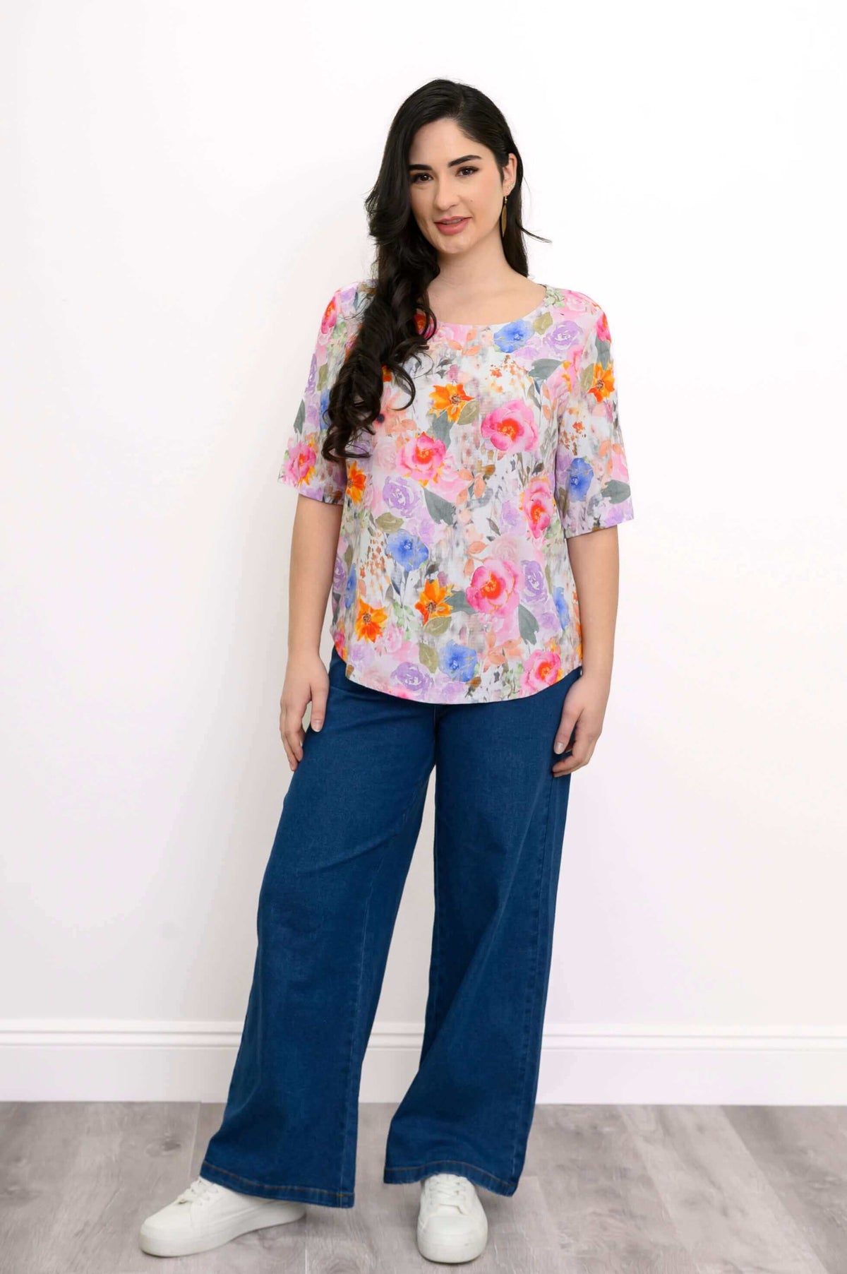 Woman standing in floral blouse and jeans, relaxed fit, front view