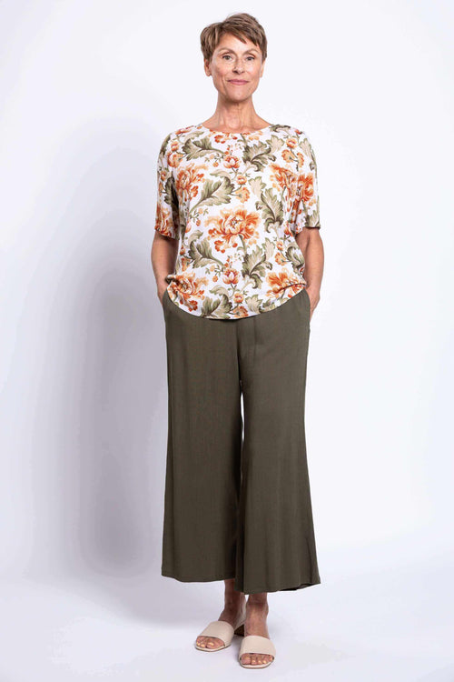 Woman wearing floral blouse and olive wide-leg pants, hands in pockets, front full view