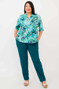 Full view of woman in blue floral blouse and teal pants, hands in pockets