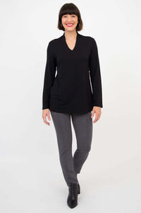 Woman modeling a black v-neck long sleeve top and grey pants, standing and smiling