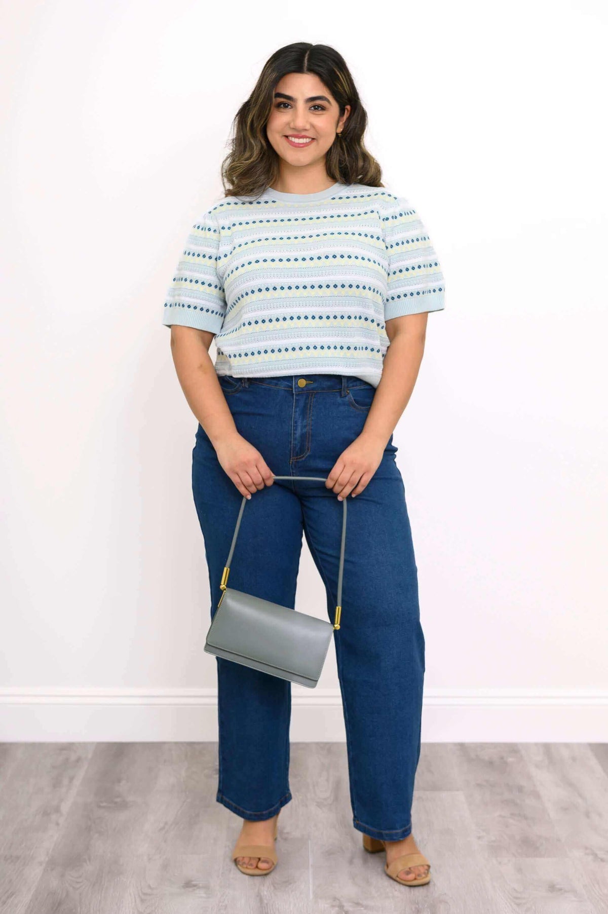 Full body view of model in Sweater and jeans holding a gray purse