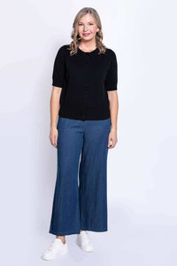 Full body view of a woman in a black buttoned cardigan, blue wide-leg pants, and white sneakers