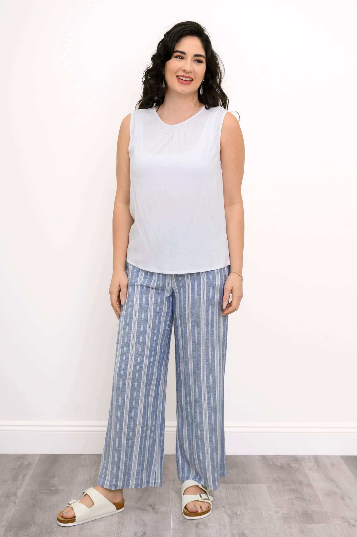 Full body view of a woman in a white sleeveless tank and blue striped wide-leg pants