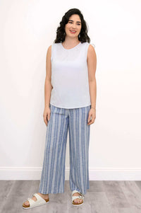 Full body view of a woman in a white sleeveless tank and blue striped wide-leg pants