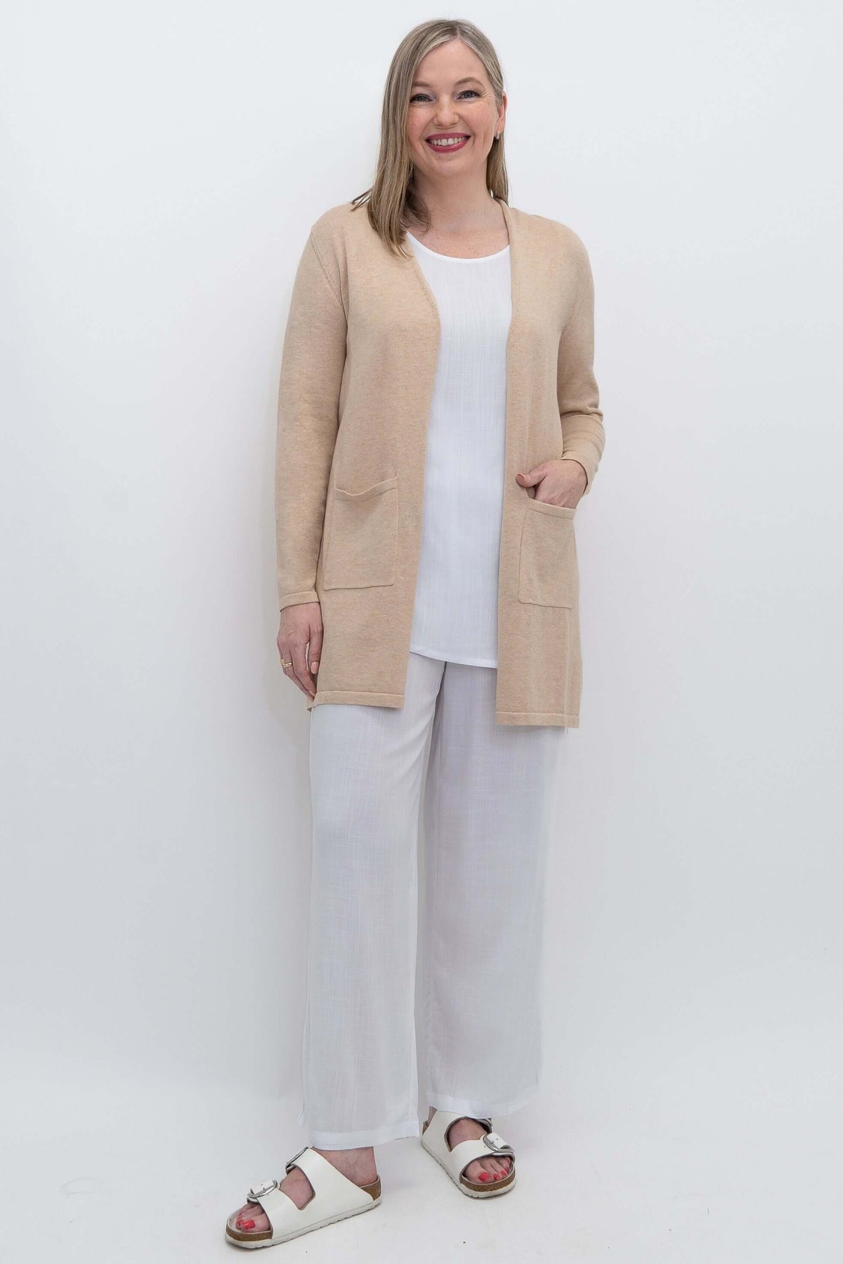 Full body view of woman in knitted beige open cardigan and white outfit