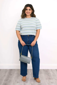 Woman in light blue sweater and blue jeans holding a gray purse, full length view