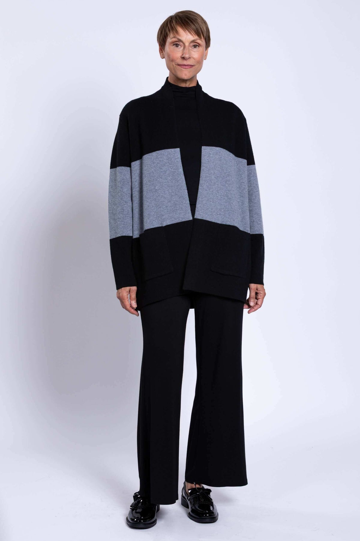 Full body view of woman in two-tone black and grey sweater and black trousers