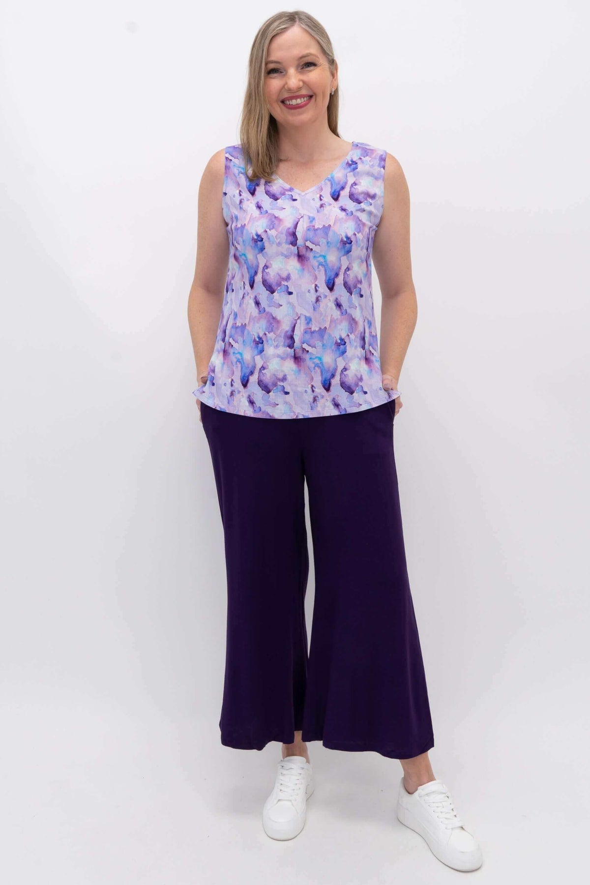 Full view of woman in watercolor V-neck tank and purple pants, hands in pockets