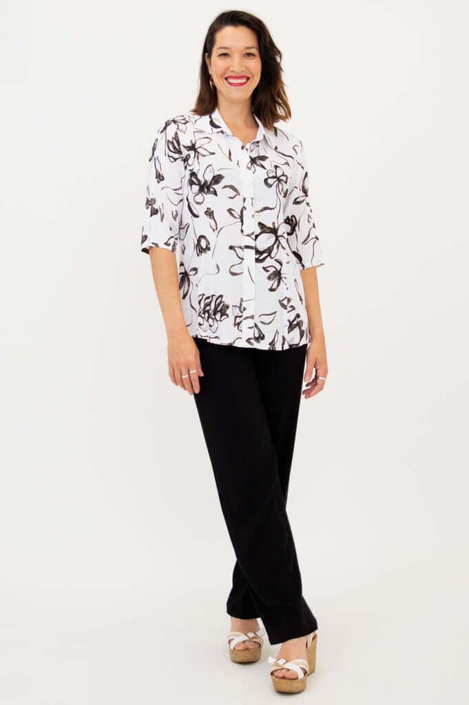 Full body view of woman in white and black floral blouse with black pants and sandals