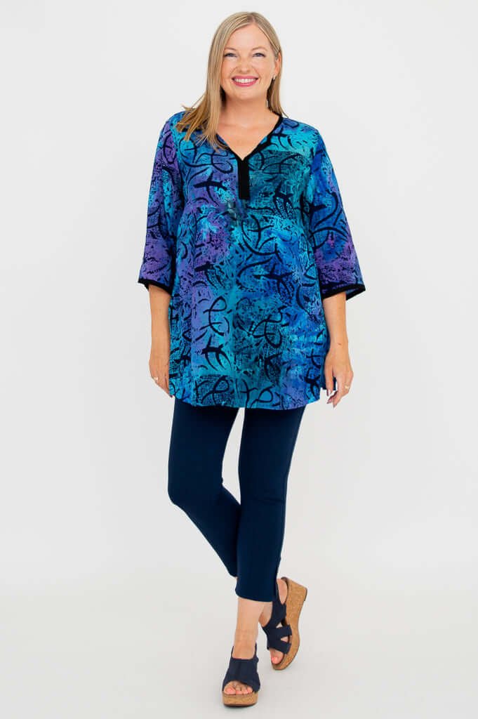 Full body view of woman in a blue and purple batik tunic blouse, navy pants, and sandals