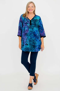 Full body view of woman in a blue and purple batik tunic blouse, navy pants, and sandals