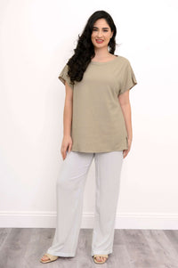 Full-length front view of woman in taupe tee and white trousers on wooden floor