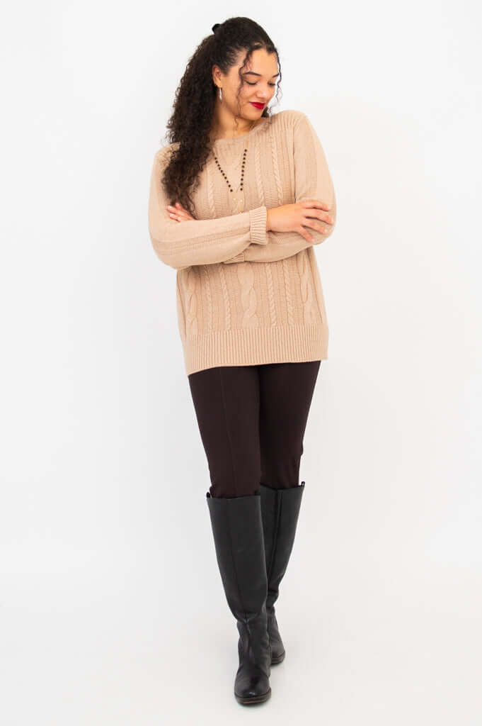 Full body view of woman in beige sweater, dark pants, and knee-high boots