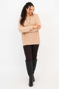 Full body view of woman in beige sweater, dark pants, and knee-high boots