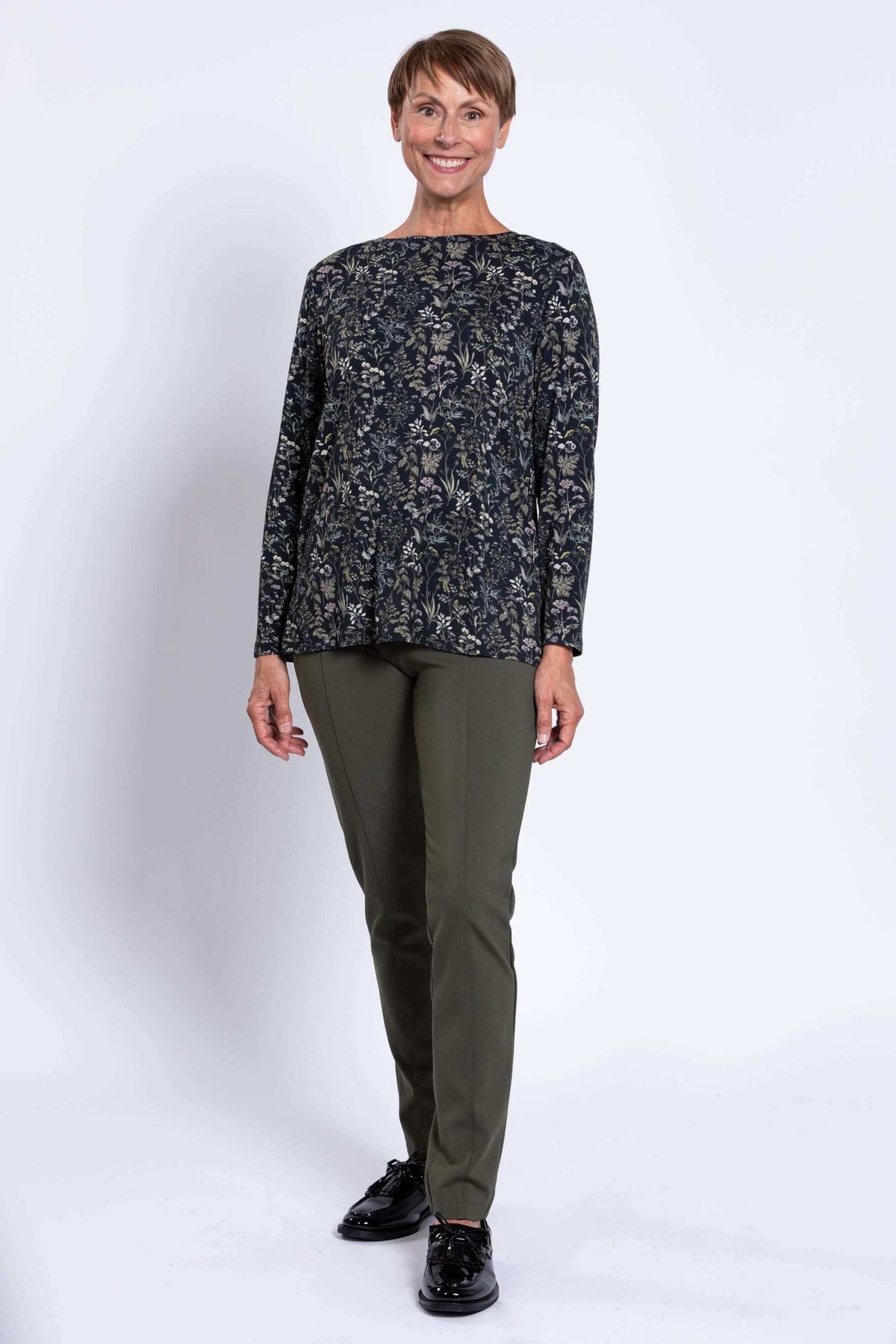 Full view of woman standing in dark floral long sleeve top and olive pants