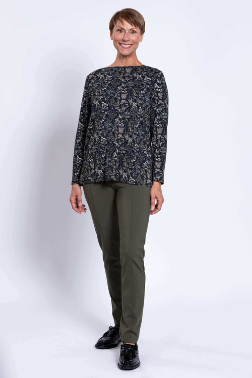 Full view of woman standing in dark floral long sleeve top and olive pants