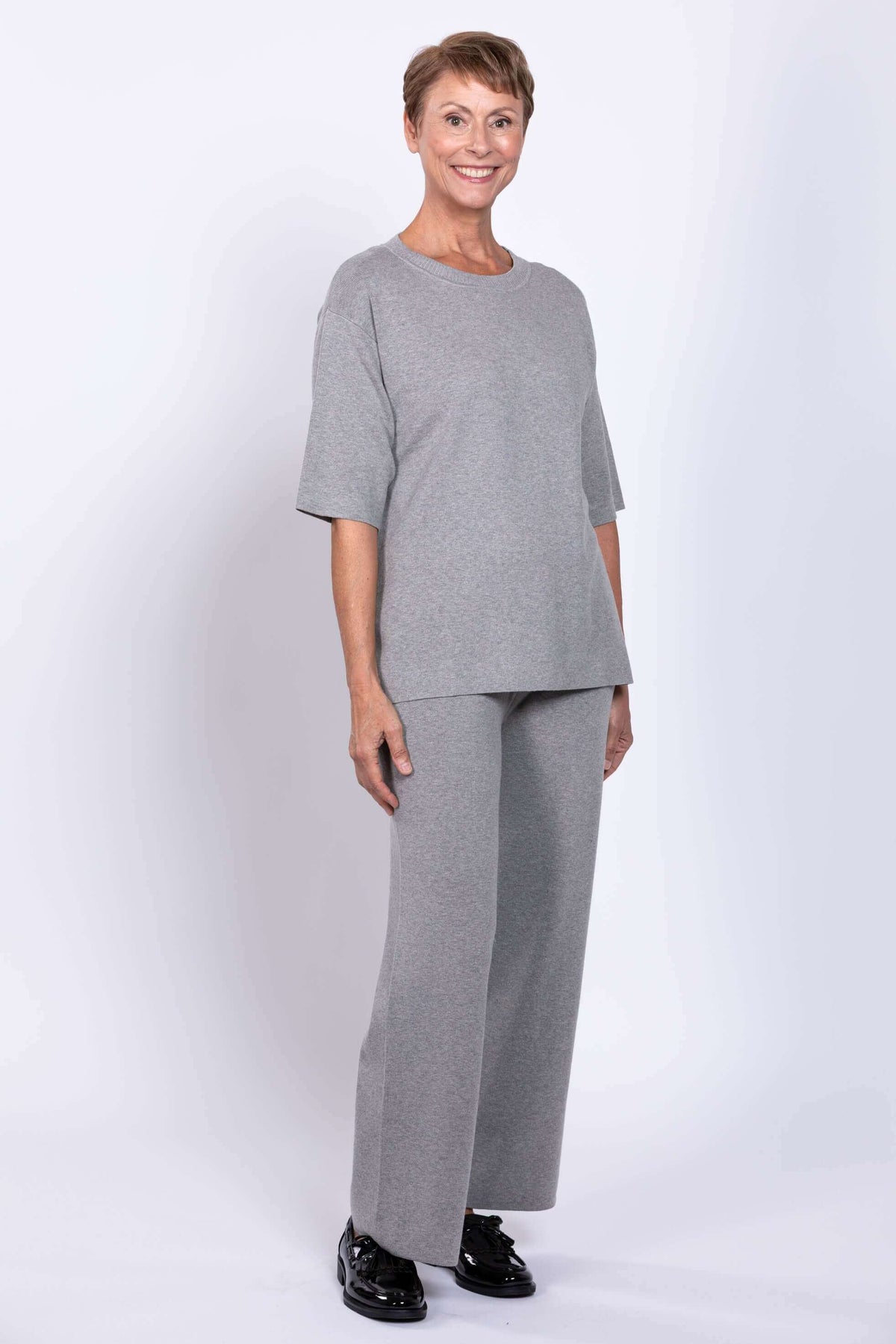 Model wearing full Bailey grey track pants and top set, standing and smiling