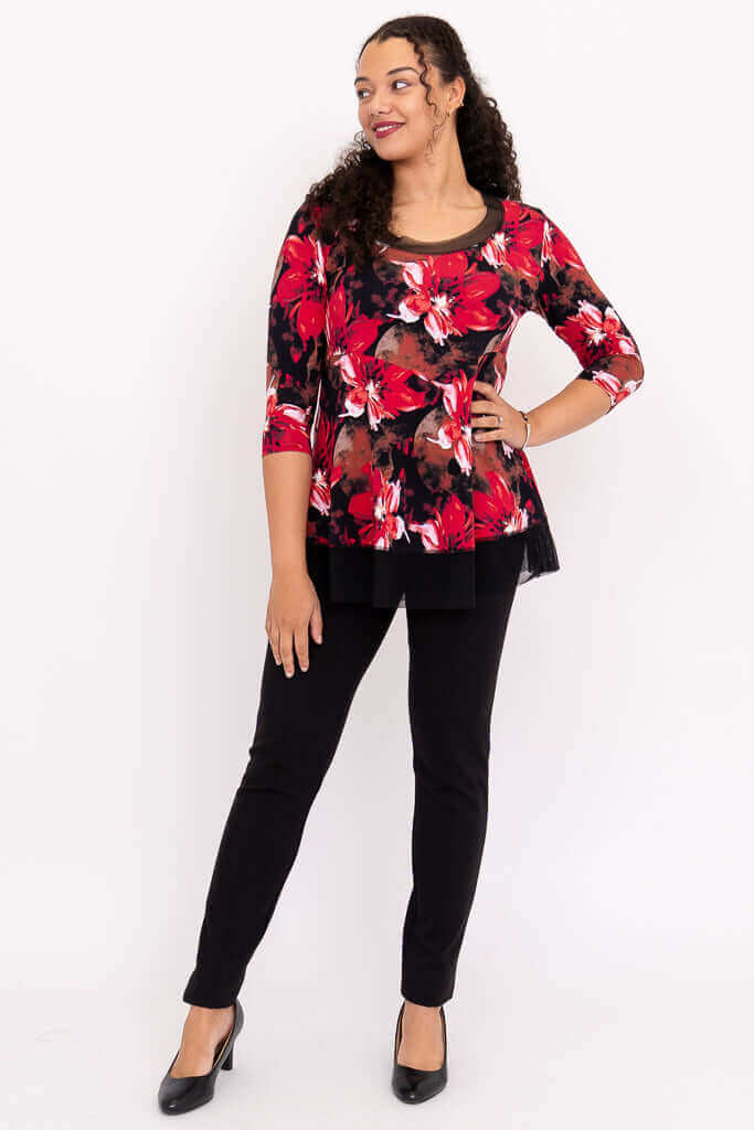 Full view of woman in black pants and red floral top with mesh details, facing forward