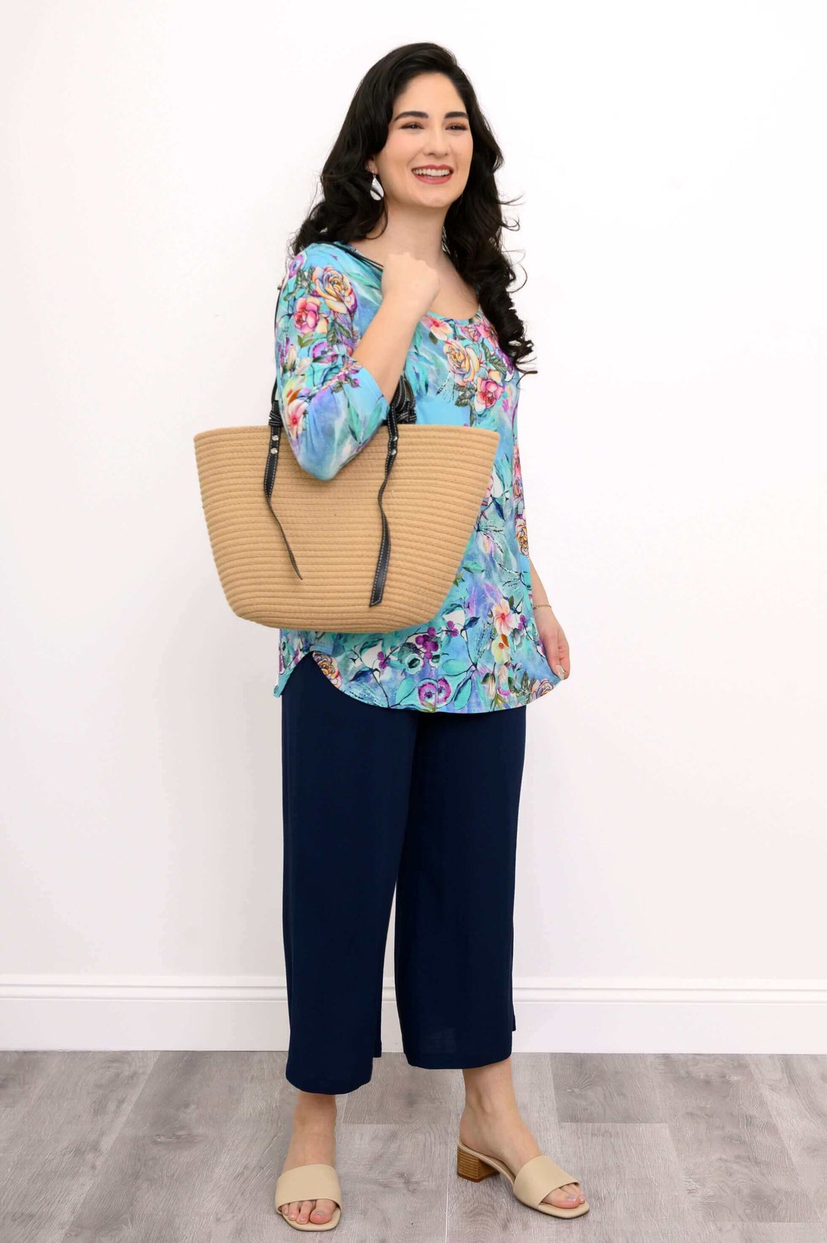 Woman modeling blue floral bamboo top, holding a straw bag, full outfit