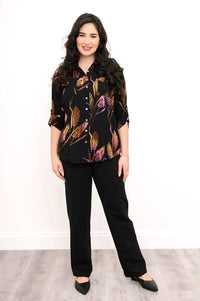 Woman standing in full view wearing a black botanical print shirt with black pants